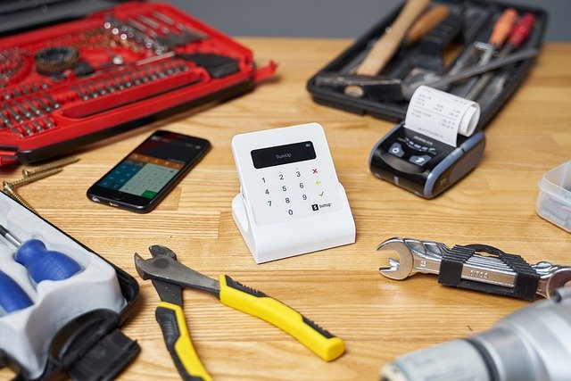 מסוף אשראי לבן על גבי שולחן, ומסביבו מכשיר סלולרי וכלי עבודה שונים