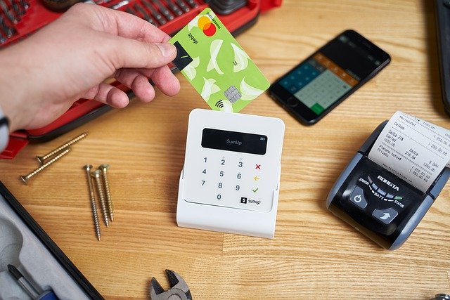 אדם מעביר כרטיס אשראי לחיוב, על גבי השולחן יש ברגים, מכשיר סלולרי וכלי עבודה
